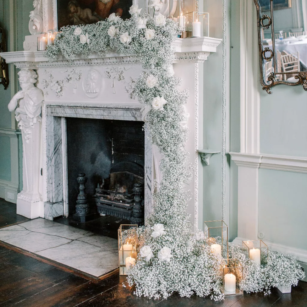 Georgian fireplace decorated with Shades of green wedding inspiration and gypsophila. A cascading floral display of gypsophila and white roses. Lit candles surround the fireplace also.