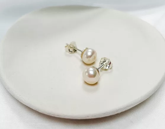 Pearl stud earrings on a cream clay dish.
