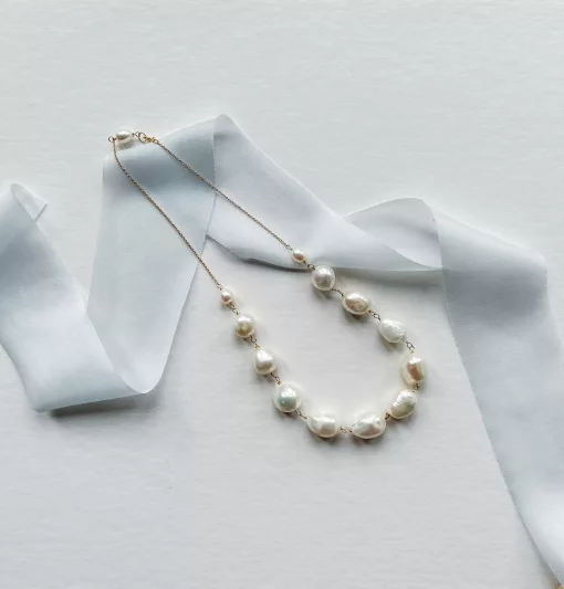 Chunky large baroque pearl bridal necklace set on a cream flat background with light blue silk ribbon.