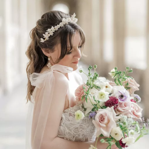 A bride stands underneath arches in Paris. She holds a bouquet of flowers and wears a bridal leaf and floral crown with statement earrings