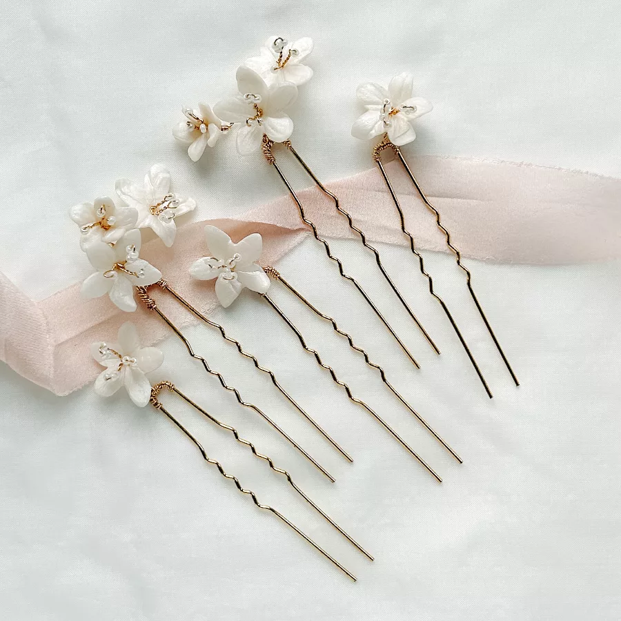 delicate wedding flower hair pins for buns lying flat on ivory fabric with blush pink ribbon