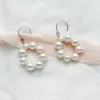 large pearl circle wedding earrings laying on blush pink silk ribbon, and an ivory fabric.