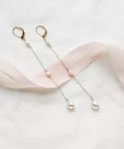 long drop pearl bridal earrings lying on a soft ivory material with blush ribbon draped across
