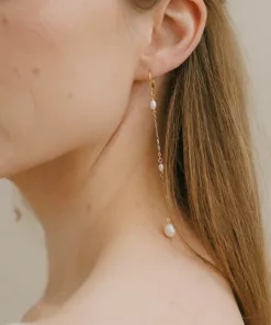 Long drop pearl bridal earrings being worn by a woman with long straight dark blonde hair. It shows a close up of the earrings, against her neck.