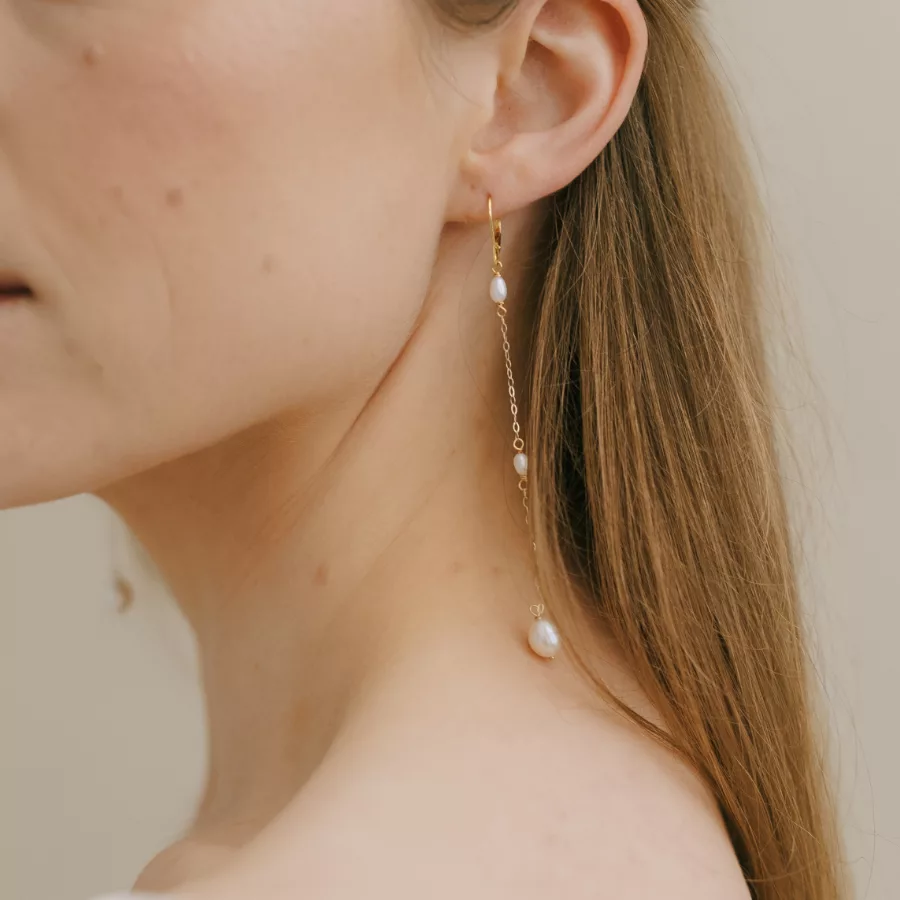 Long drop pearl bridal earrings being worn by a woman with long straight dark blonde hair. It shows a close up of the earrings, against her neck.