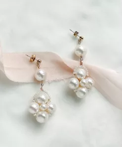 luxury large real pearl drop earrings with gold studs laying on an ivory fabric background with blush pink ribbon