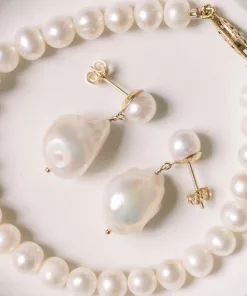 luxury pearl drop bridal stud earrings laid on a cream backdrop inside a pearl bracelet