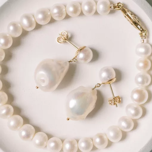luxury pearl drop bridal stud earrings laid on a cream backdrop inside a pearl bracelet
