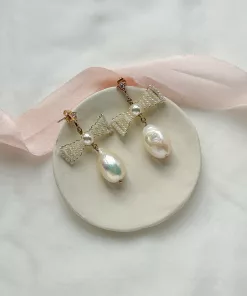 pearl bow wedding earrings set on a cream clay flat bowl on an ivory fabric with blush pink silk ribbon.