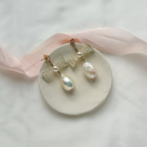 pearl bow wedding earrings set on a cream clay flat bowl on an ivory fabric with blush pink silk ribbon.