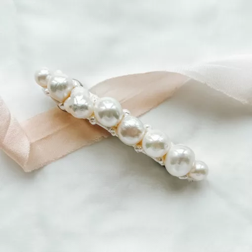pearl bridal hair clip for shorter hair laying on an ivory fabric background with blush pink ribbon to decorate