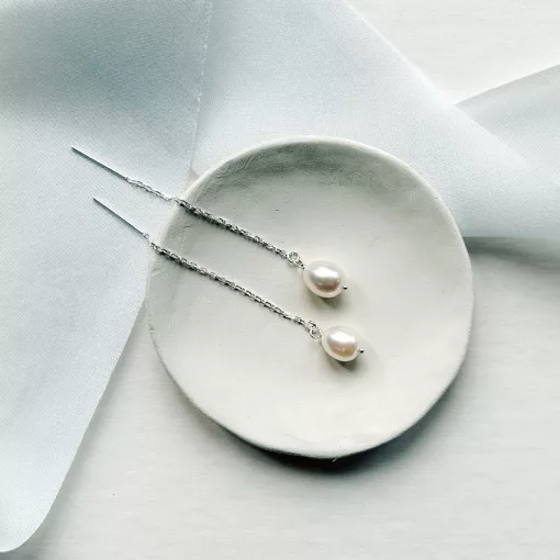 threader chain Long pearl bridal earrings set on a small cream dish. It sits on a while background with light blue silk ribbon.