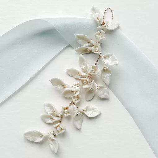 Bridal updo wedding hair vine with clay leaves and pearls resting on a plain white background with light blue silk ribbon.