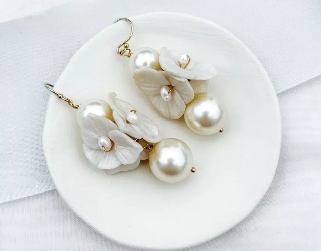 Modern statement bridal earrings with flowers and pearls set on a small cream clay dish and white background with light blue silk ribbon