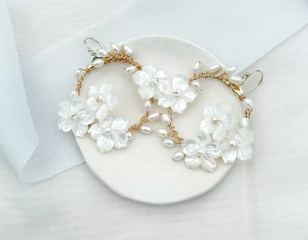 Modern statement bridal earrings with flowers and pearls set on a small cream clay dish and white background with light blue silk ribbon